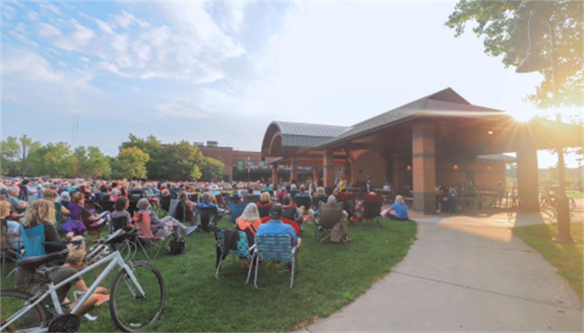 A crowed of community members sit outside on a sunny evening enjoying an outdoor concert at the Haffeman Pavilion.