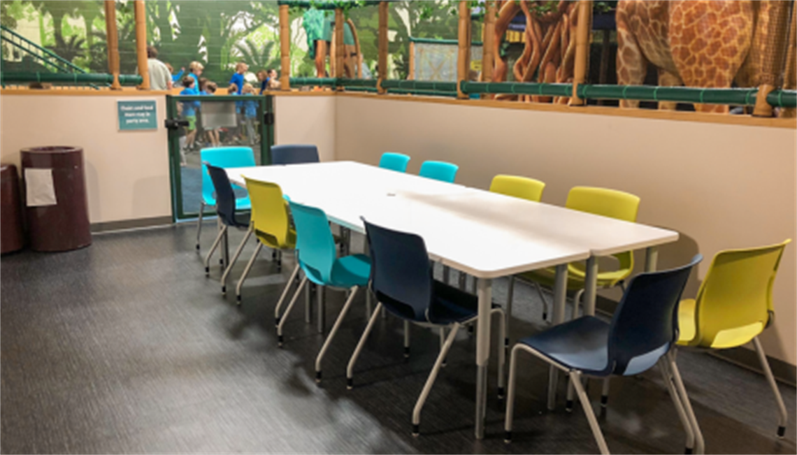 Indoor playground party space includes a table with brightly colored chairs